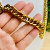 Cadena dorada estilo cubano sostenida en la mano para mostrar detalles.