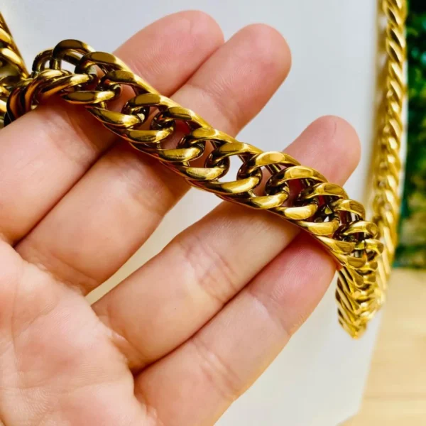 Cadena dorada estilo cubano sostenida en la mano para mostrar detalles.