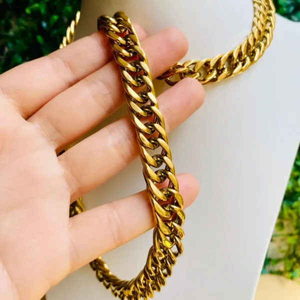 Cadena dorada con eslabones anchos sostenida en la mano.